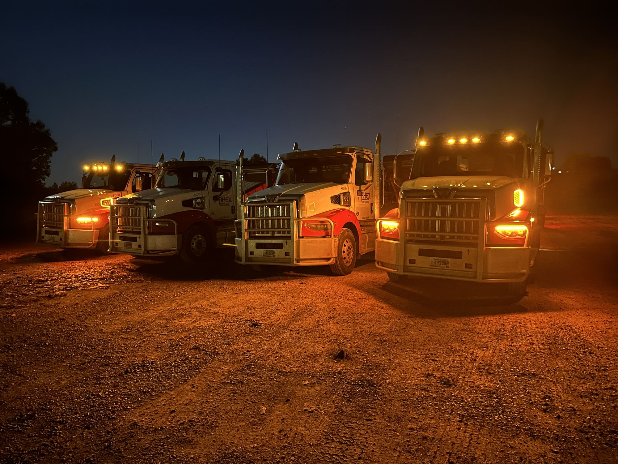 Four trucks parked at night with amber lights on