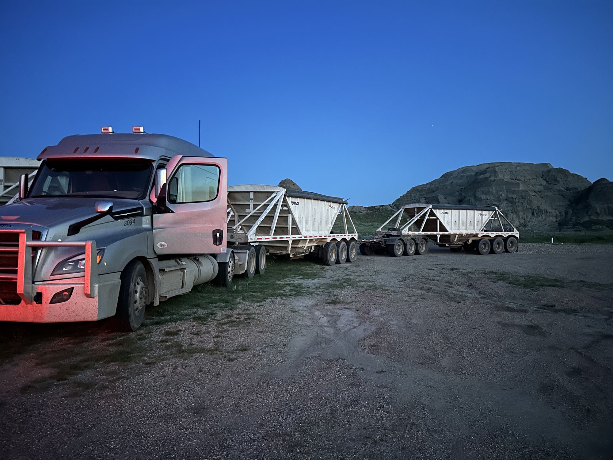 Truck and sand trailers at dusk with hills behind