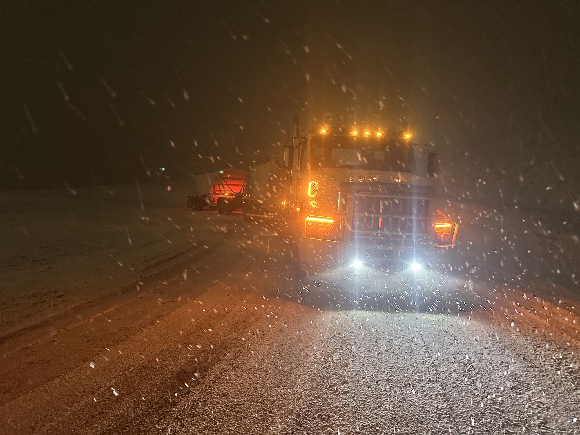 Truck driving through snow at night